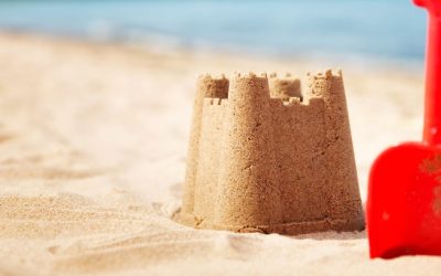Sandcastle with a shovel on the sea in summertime. Seashore on beautiful day. Sand on the beach and blue water